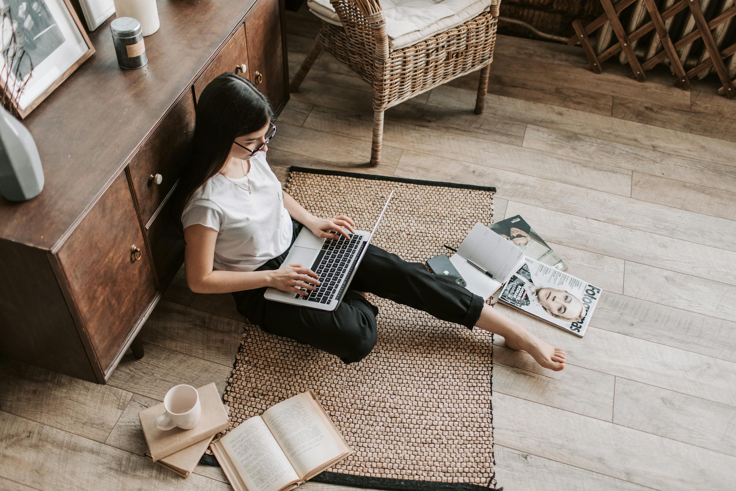 Confident young businesswoman with laptop and notebook sitting on floor modern apartment